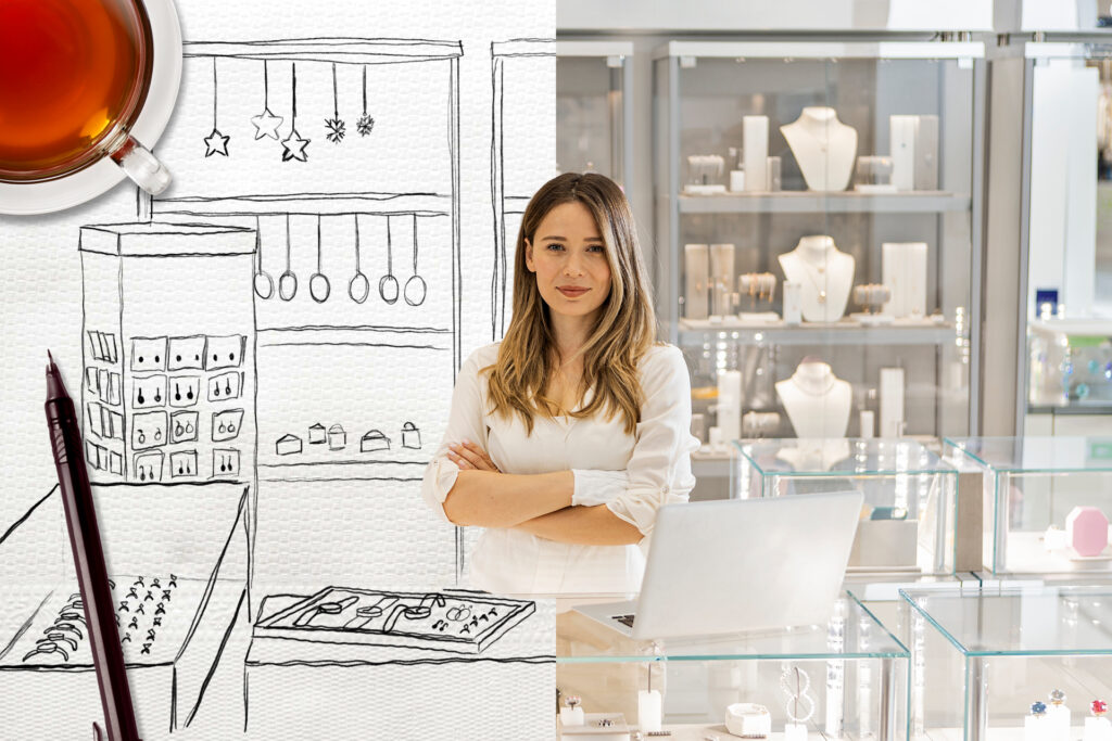 A jewellery owner stands proudly behind her glass display. She is surrounded by articles of luxury jewellery. The left hand side of the scene shows a sketch of the scene on scrap paper with a pen and cup of tea overlaid. The right hand side shows the real scene as a photograph.